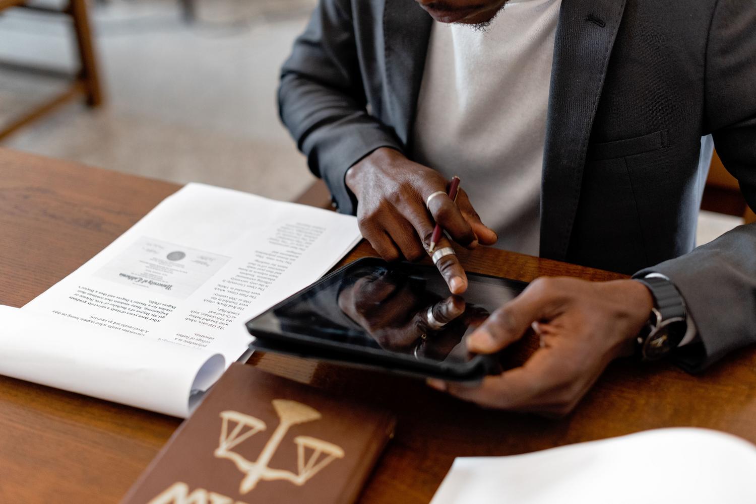 Profesional utilizando una tablet digital junto a documentos legales, ilustrando la digitalización de los procesos regulatorios. Profesional utilizando una tablet digital junto a documentos legales, ilustrando la digitalización de los procesos regulatorios.