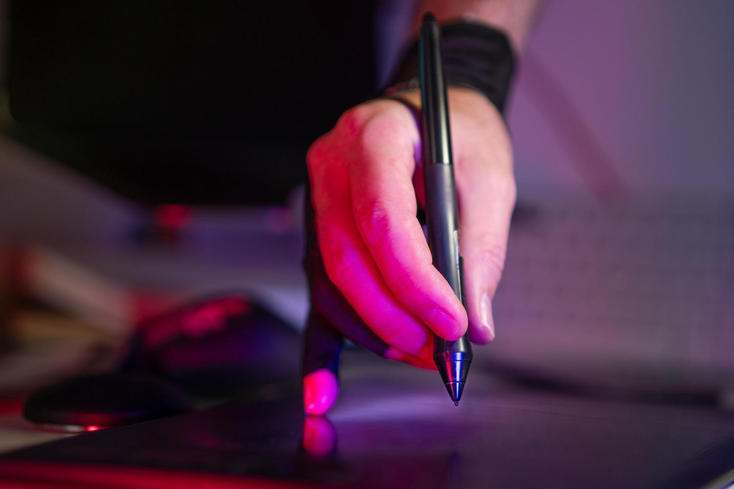 Detalle de una mano con guante de dibujo profesional utilizando un lápiz óptico sobre una tableta digital con iluminación artística.