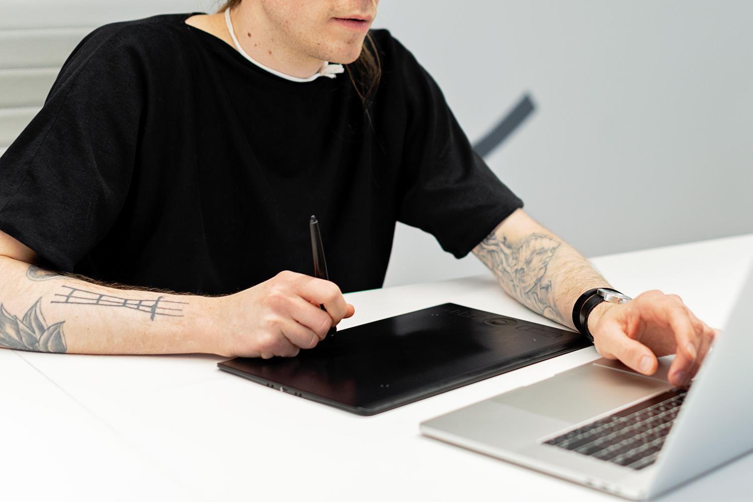 Un artista digital trabajando con una tableta gráfica y un portátil en un entorno de estudio iluminado.