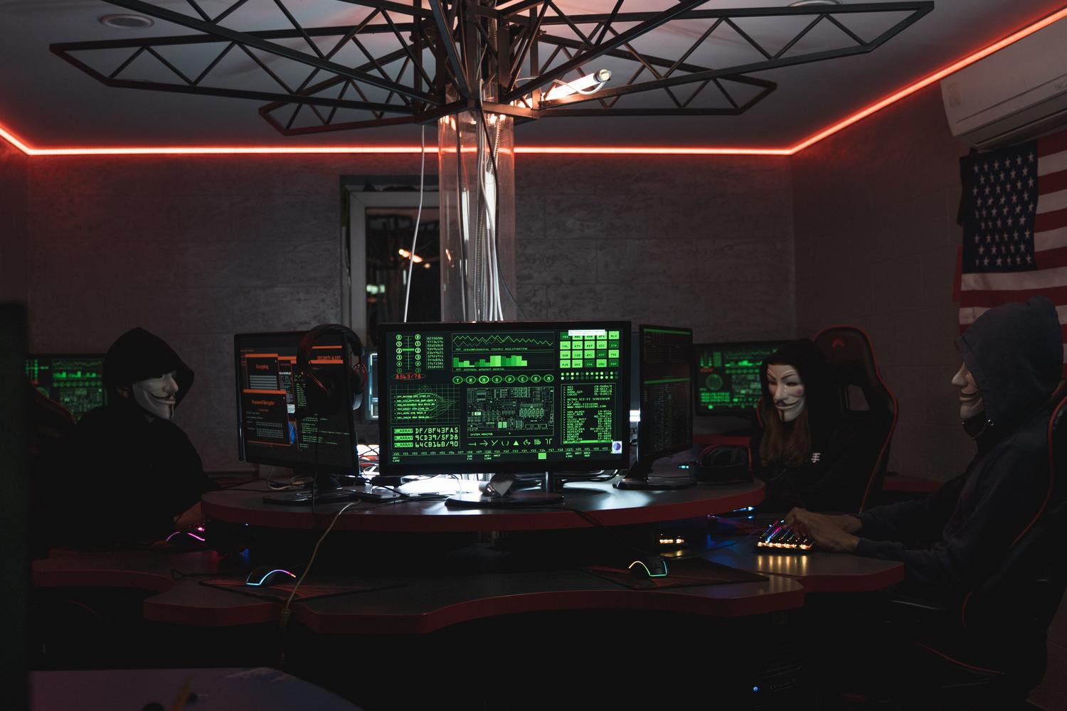 Ciberdelincuentes con máscaras operando en una sala oscura, representando amenazas comunes como el ransomware y el phishing. Ciberdelincuentes con máscaras operando en una sala oscura, representando amenazas comunes como el ransomware y el phishing.