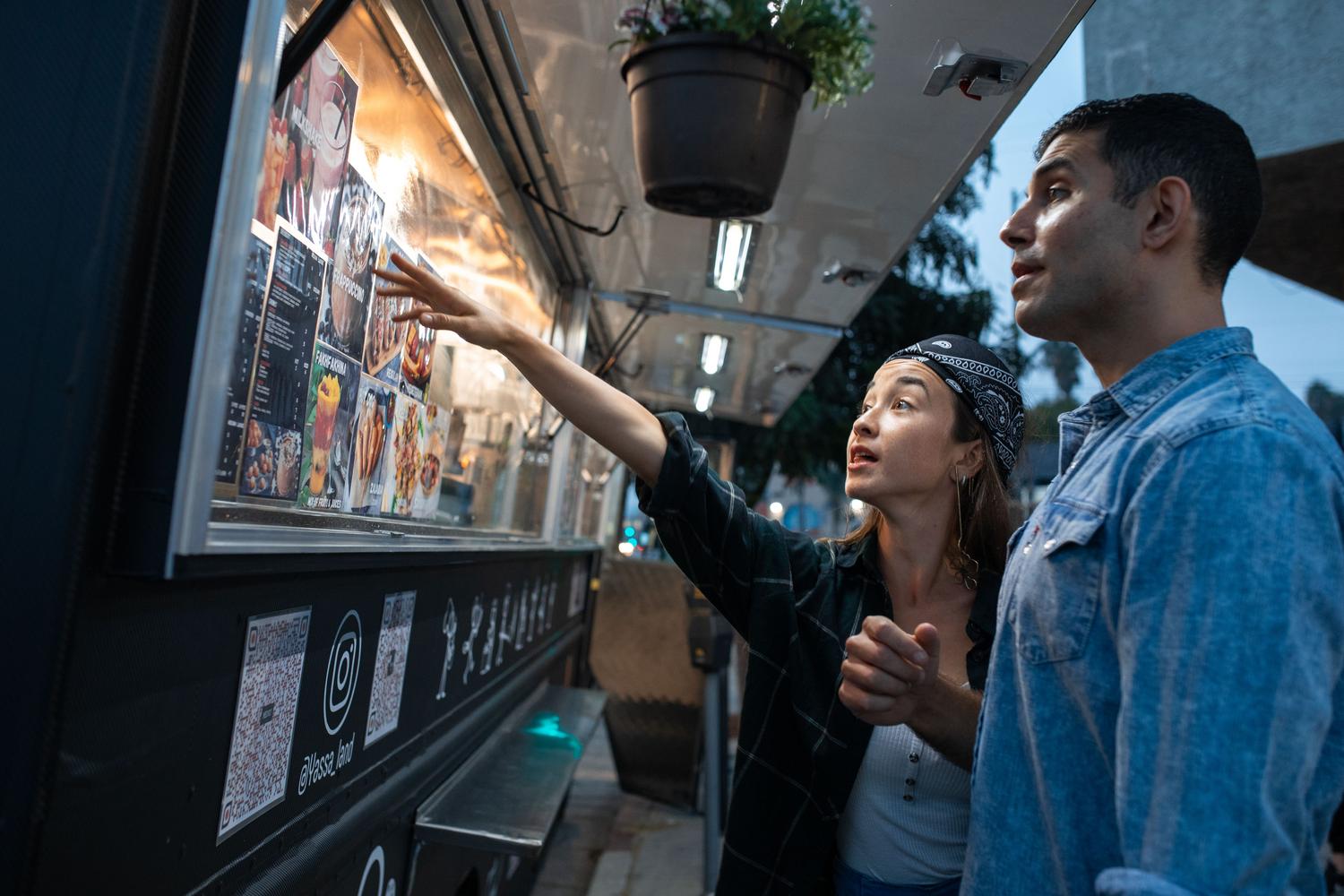 Pareja consultando la carta visual y colorida de un food truck nocturno.