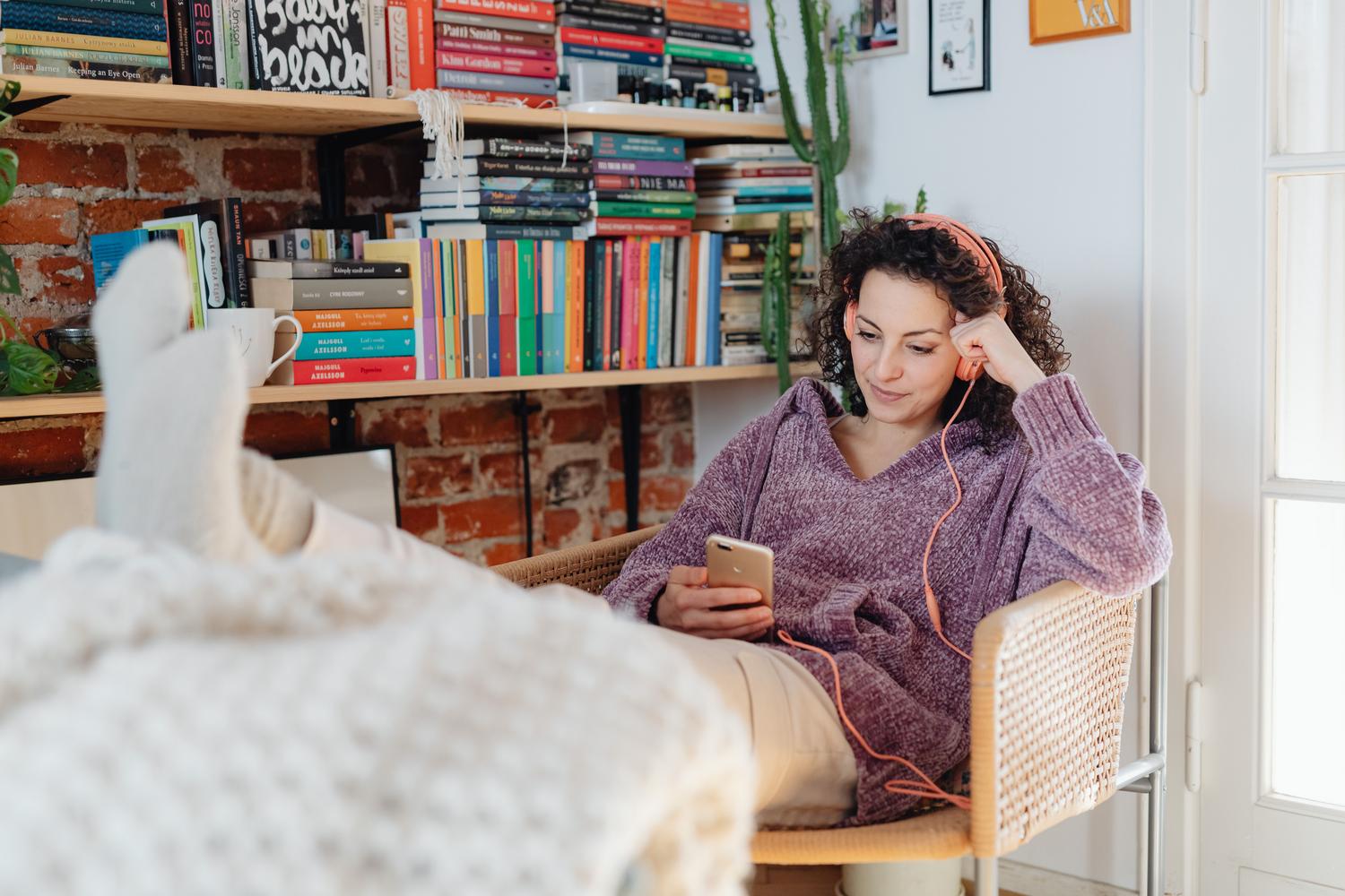 Una mujer relajada en casa escuchando música con auriculares y un smartphone, ilustrando la comodidad del acceso remoto.
