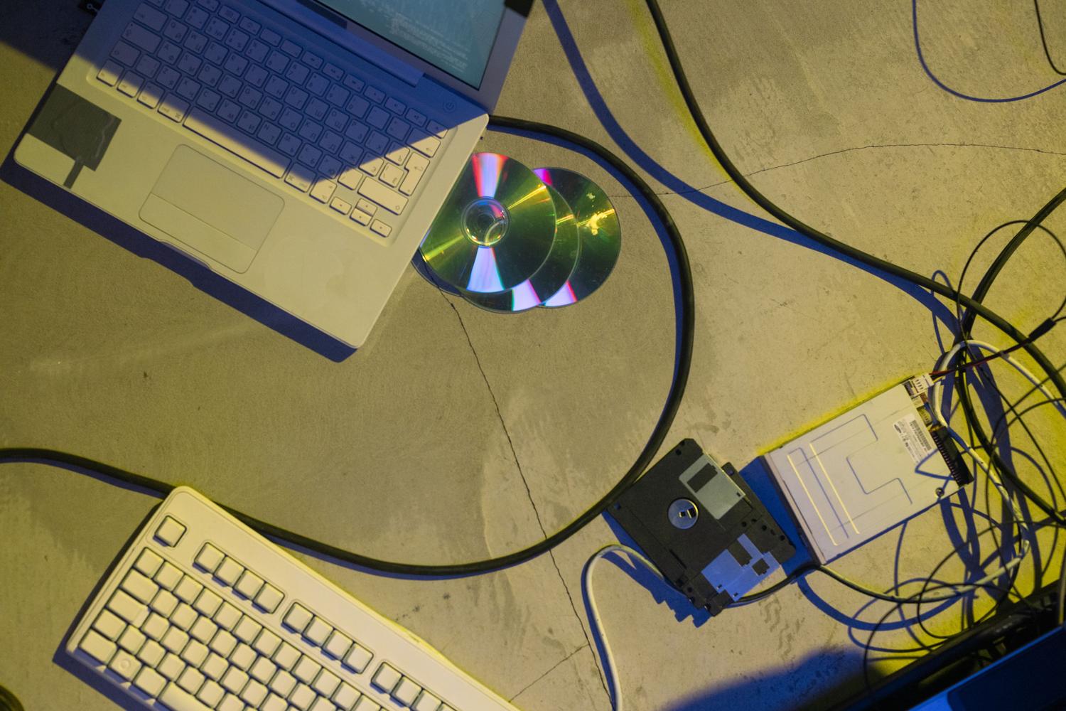 Accesorios de computación vintage como disquetes, CDs y un portátil antiguo sobre un suelo de hormigón, representando el hardware obsoleto