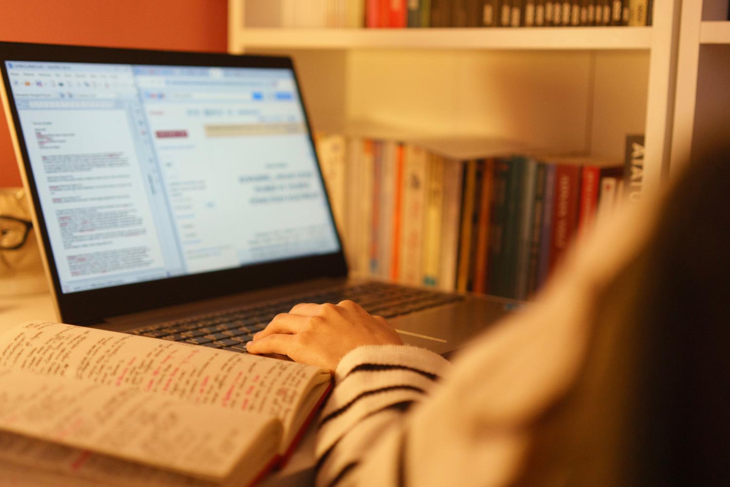 Estudiante estudiando con un ordenador portátil y un libro abierto en un ambiente acogedor