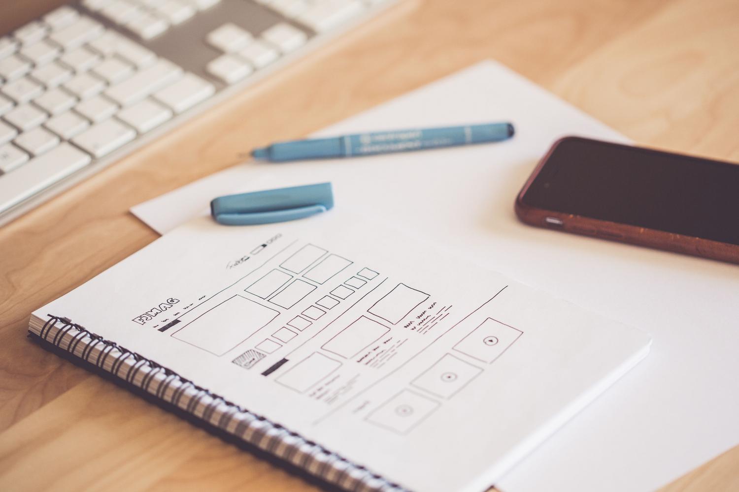 Espacio de trabajo con wireframes y bocetos en papel junto a un smartphone, representando la fase de prototipado de la experiencia de usuario.