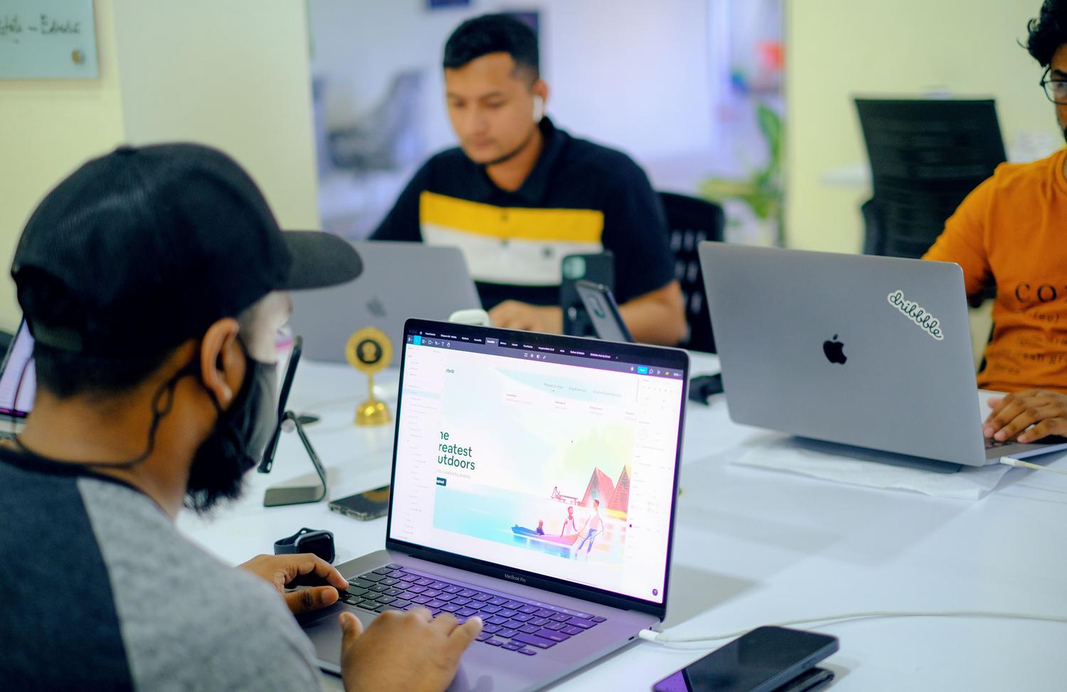 Equipo de profesionales colaborando en una oficina con laptops, ilustrando la funcionalidad de colaboración en tiempo real de Voiceflow.