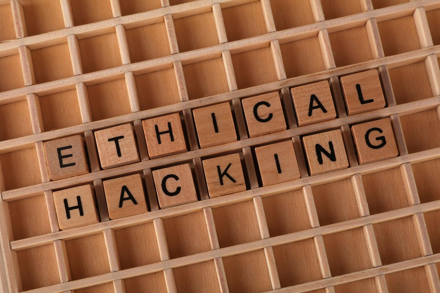 Bloques de madera formando el texto Ethical Hacking sobre un fondo tecnológico, ideal para introducir el concepto de hacking ético.