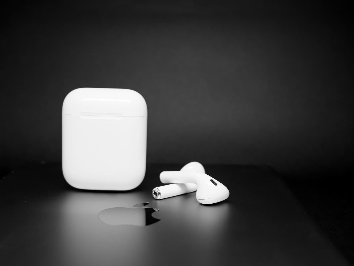 Sleek wireless earbuds and their charging case on a dark reflective surface, representing low latency and modern audio technology.