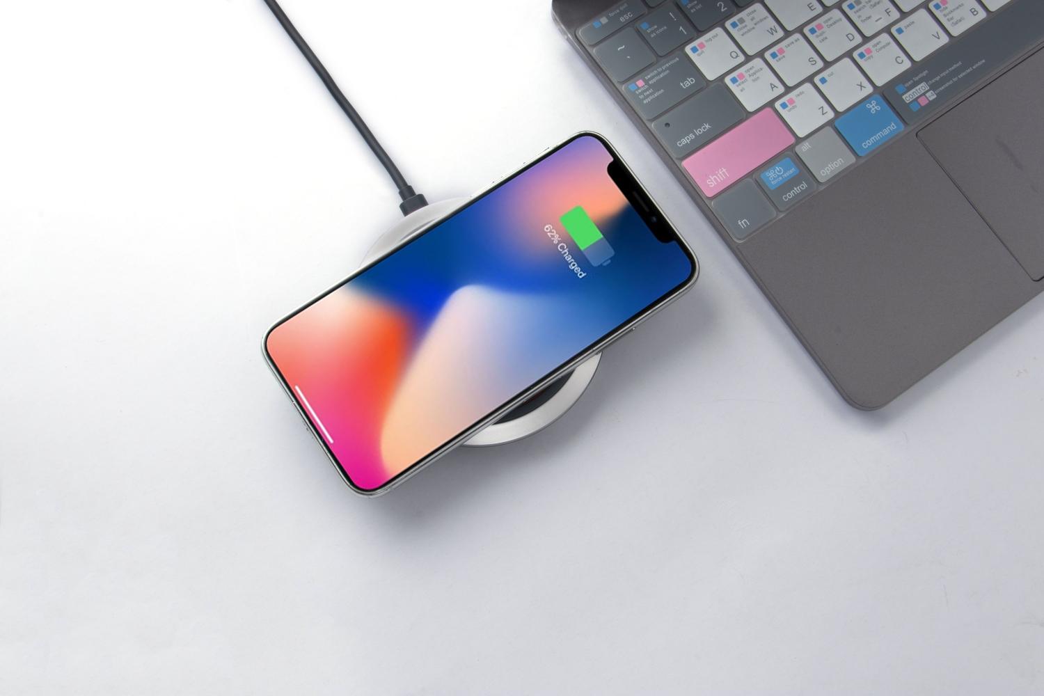 Smartphone cargando de forma inalámbrica sobre una base en un escritorio moderno junto a un ordenador portátil.