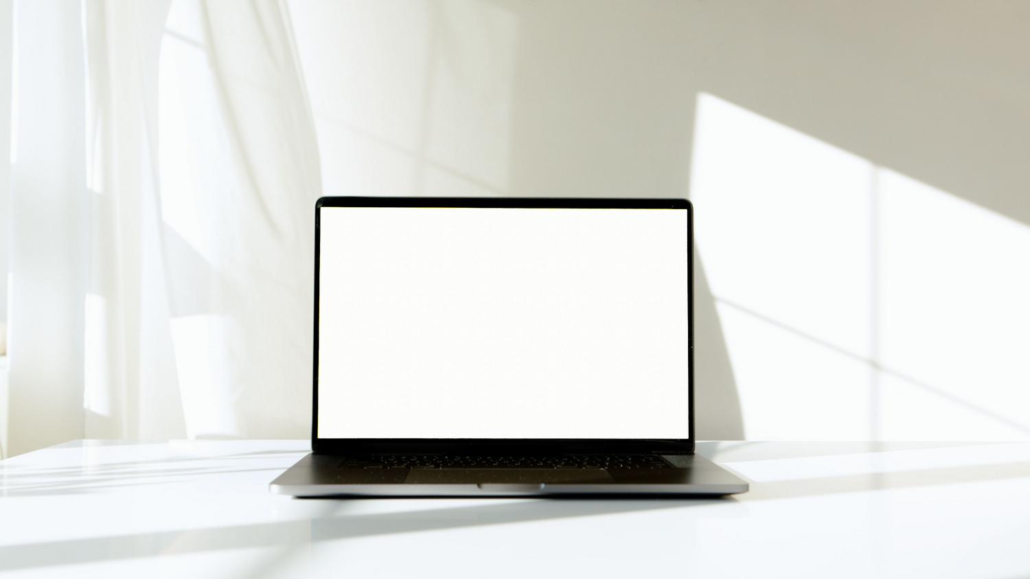 Portátil moderno con pantalla blanca en un escritorio luminoso, ideal para representar un entorno digital sin distracciones.