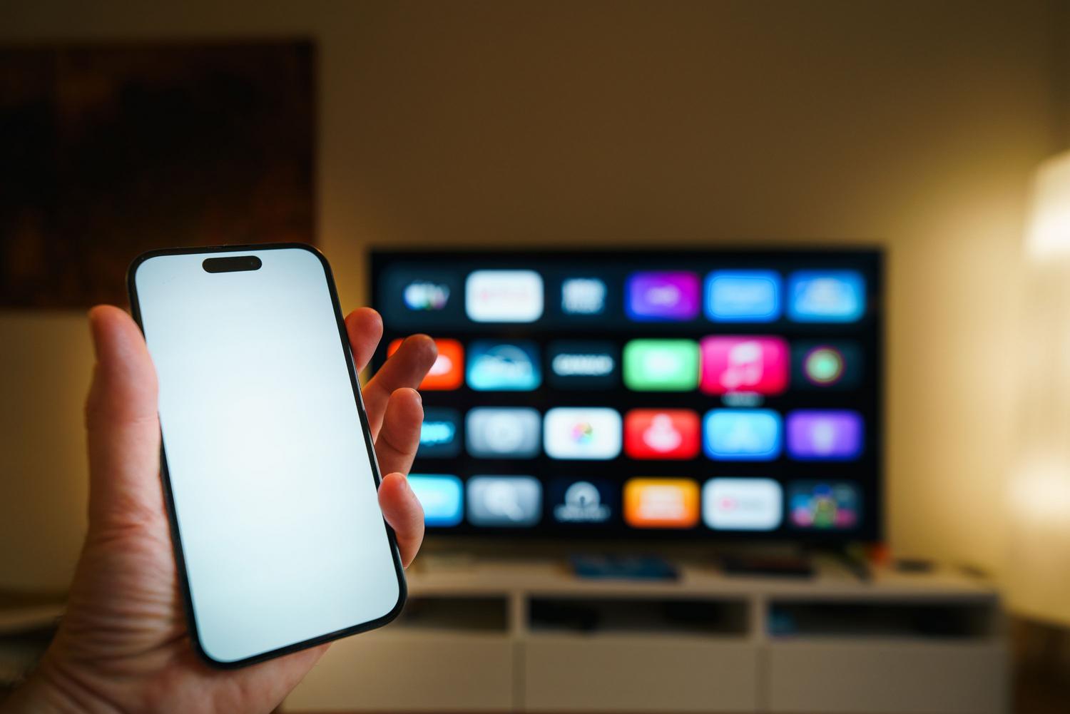 Persona comprobando la conexión a internet en su smartphone con un televisor inteligente al fondo.
