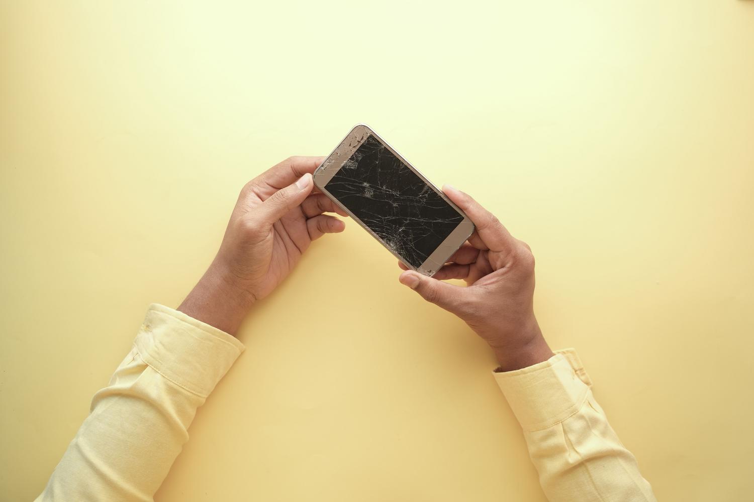 Persona sosteniendo un smartphone con la pantalla rota, ilustrando el momento del accidente.