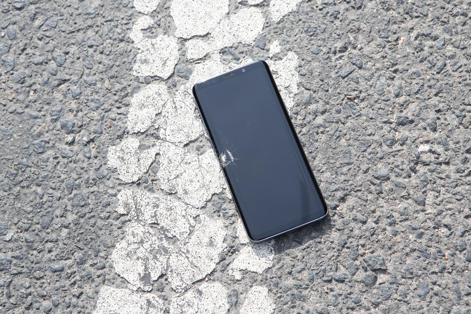 Teléfono móvil con la pantalla estrellada tirado sobre el asfalto.
