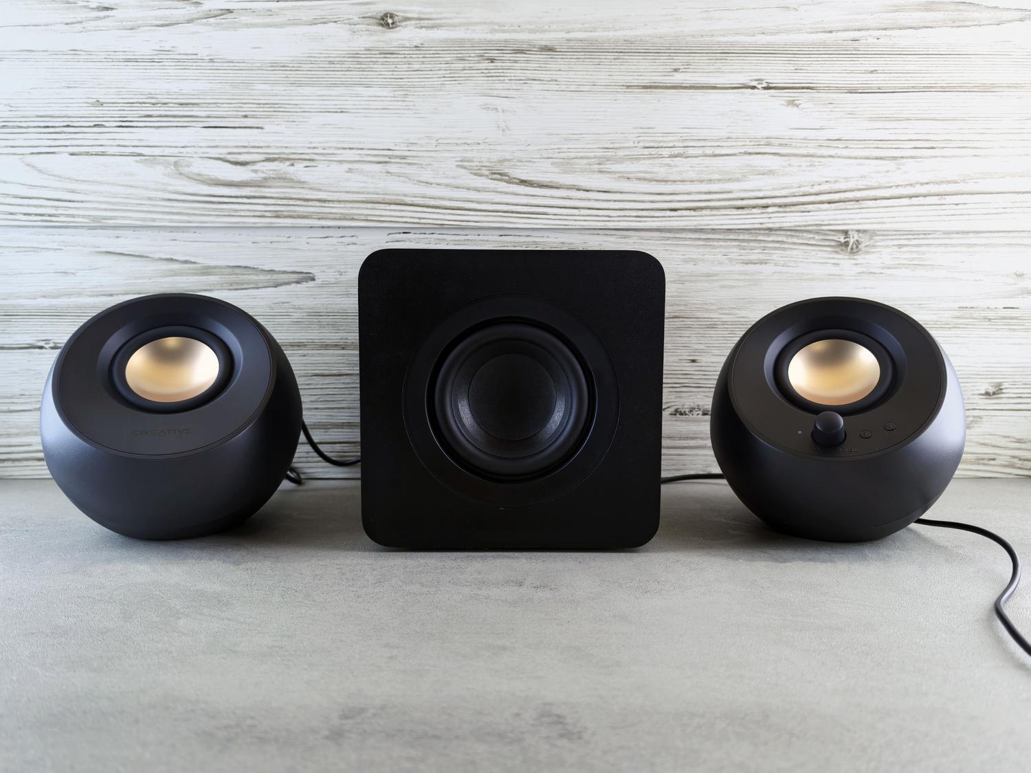 Sistema de audio 2.1 con un subwoofer central y altavoces satélite, mostrando la diferencia de tamaño y función entre los drivers de graves y medios.