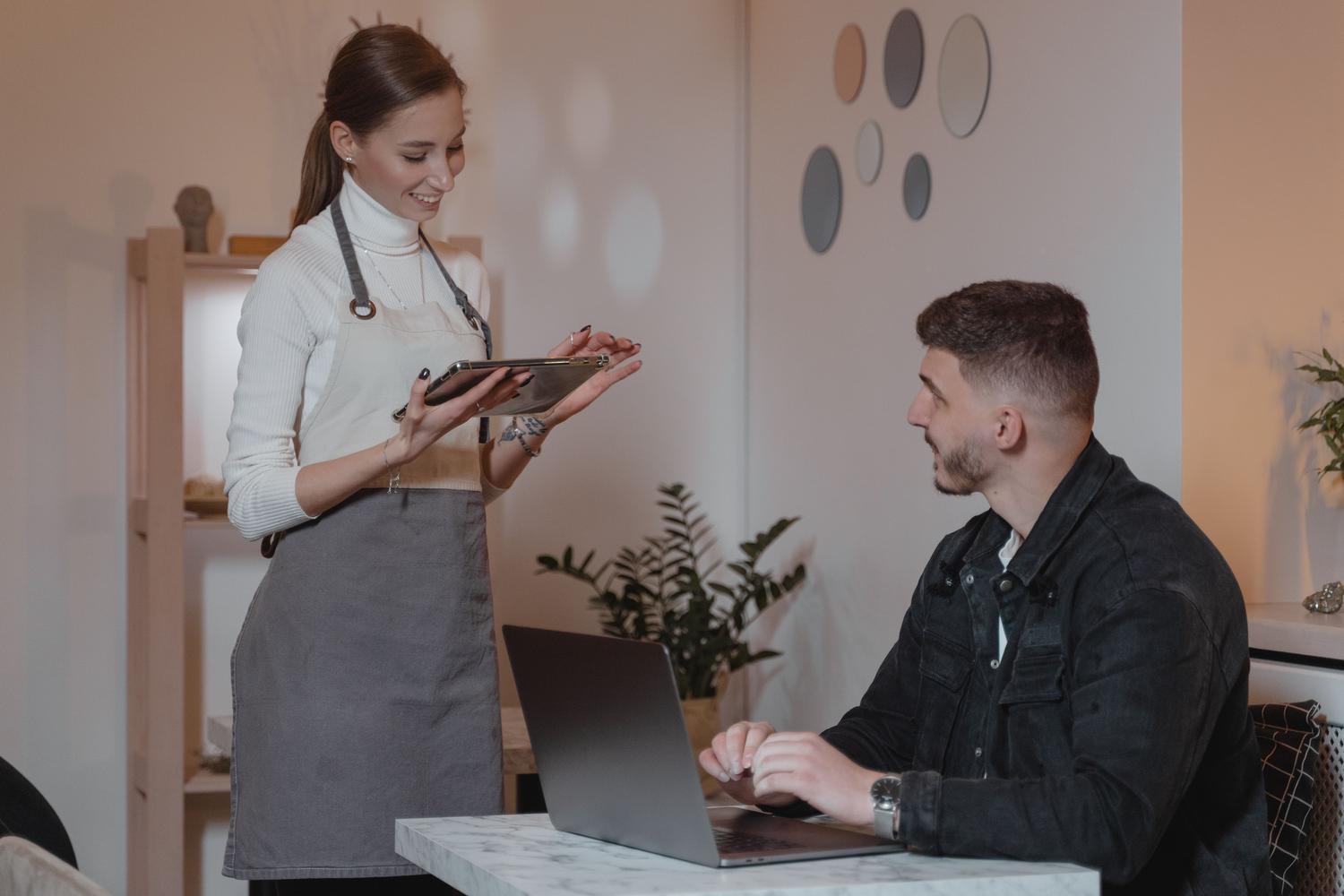 Camarera utilizando una tablet para tomar el pedido de un cliente en un café moderno, optimizando el servicio.