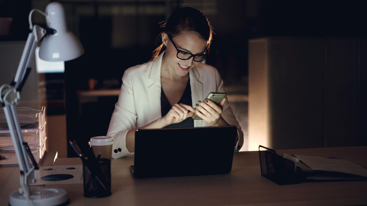 Mujer profesional utilizando su smartphone en la oficina, ilustrando la gestión de correos y productividad móvil.