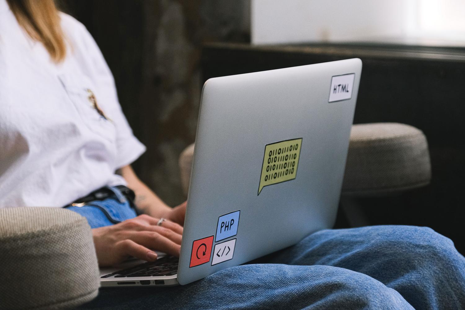 Desarrollador trabajando en un portátil con pegatinas de programación, representando el entorno de trabajo remoto y moderno.