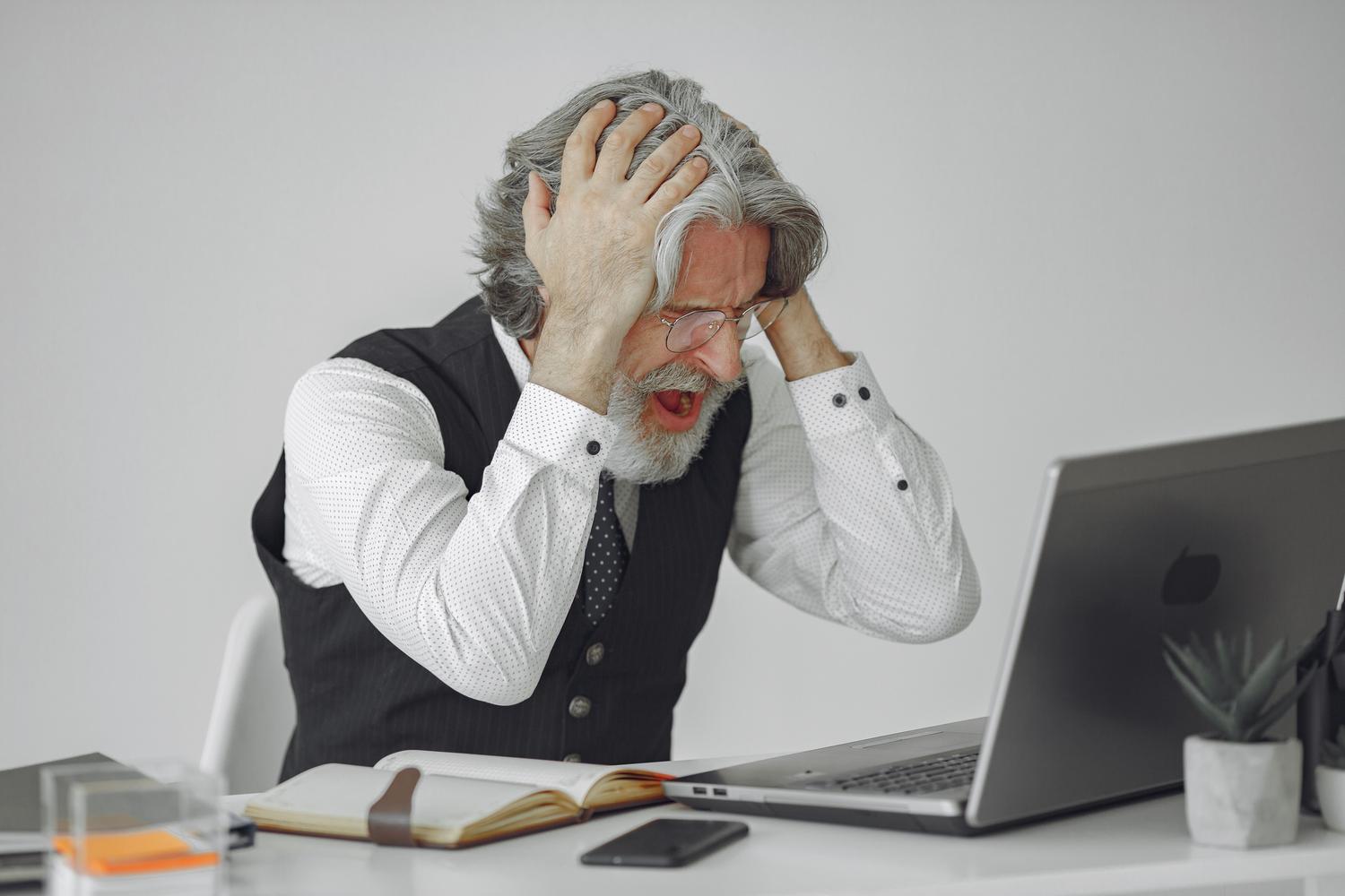 Isang bigo at desperado na propesyonal na lalaki sa harap ng kanyang laptop sa opisina, na kumakatawan sa stress ng pagkawala ng access sa isang digital account.