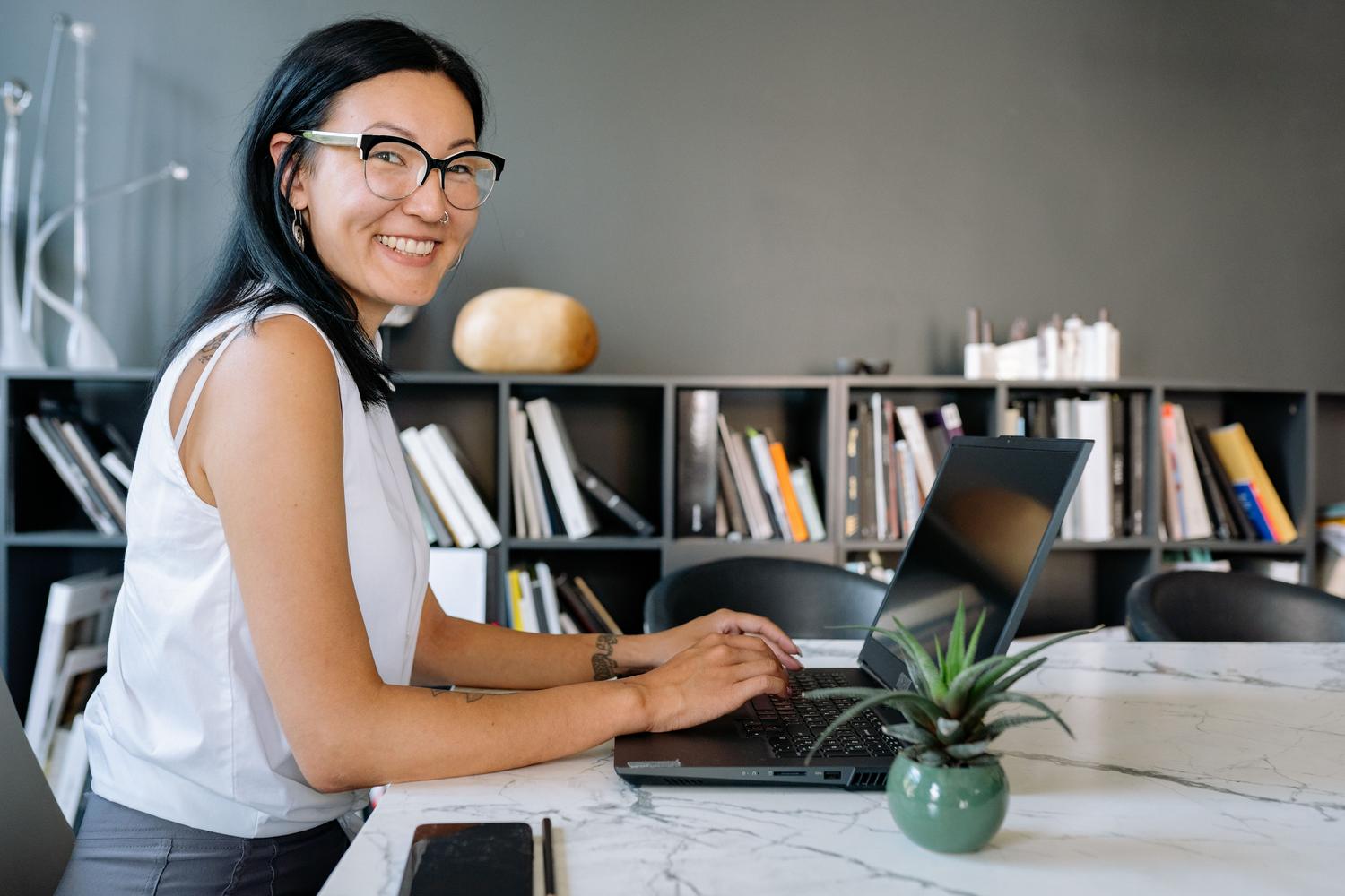 Mujer profesional trabajando en un ordenador portátil en una oficina moderna y luminosa, ideal para ilustrar la creación de reportes técnicos.