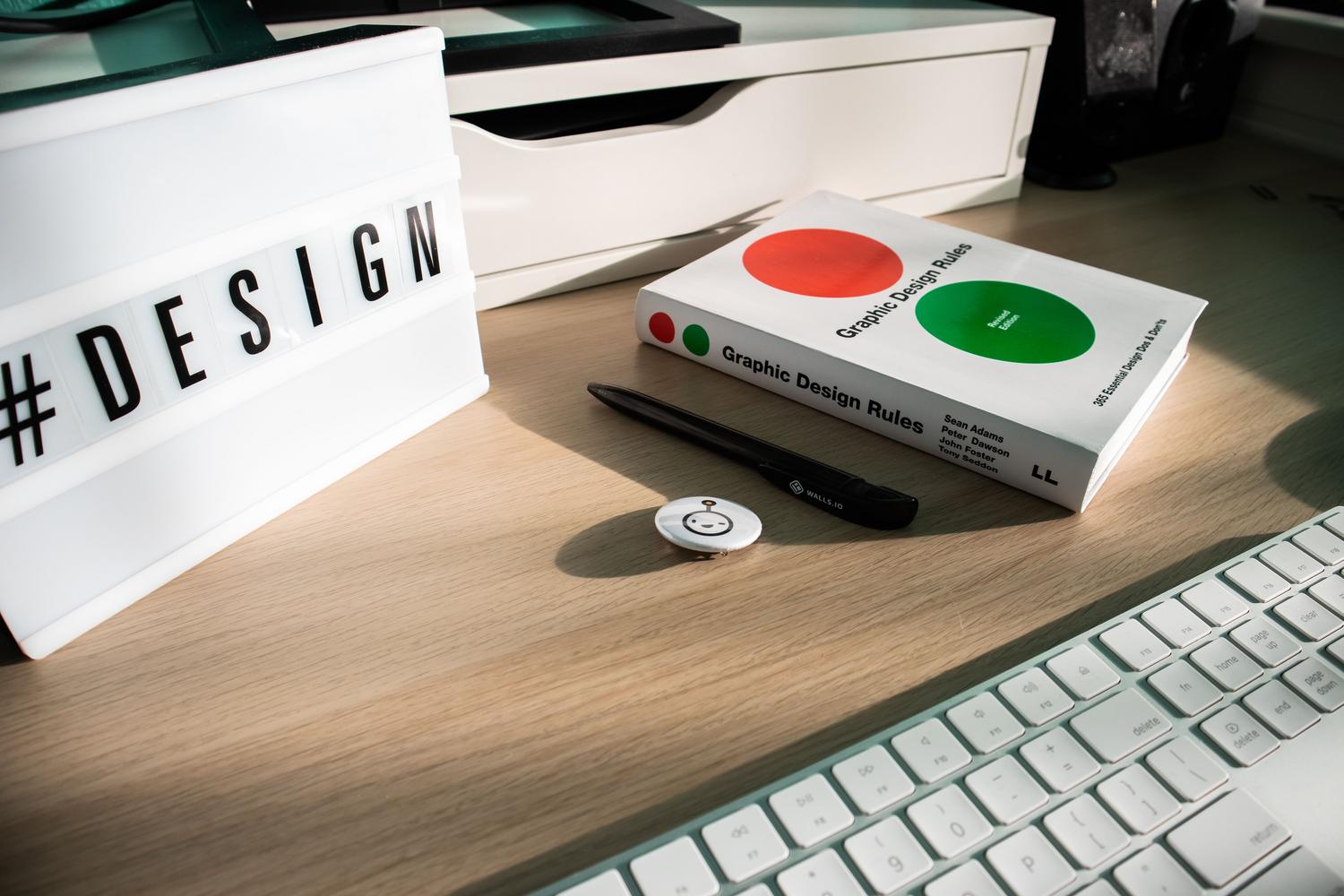 Escritorio de diseño profesional con un libro de reglas de diseño gráfico y un letrero luminoso de #DESIGN, sugiriendo la profesionalización de la maquetación.