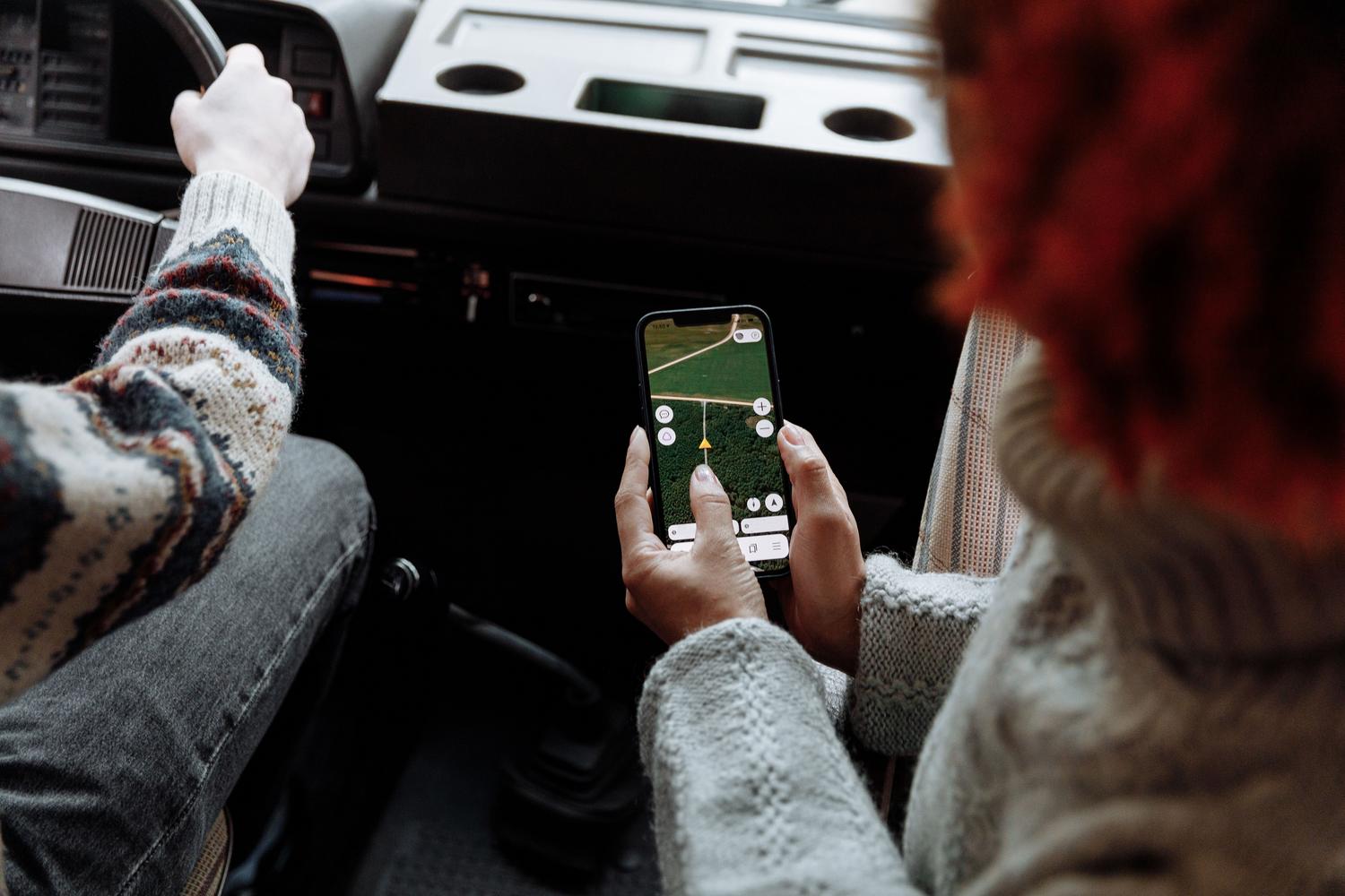 Dos personas coordinando su ruta mediante una aplicación de mapas en un smartphone durante un viaje por carretera, evocando la seguridad y compañía.