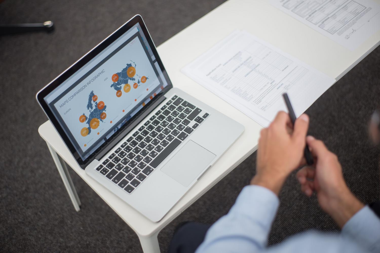 Espacio de trabajo para análisis de datos con Google Sheets Vista cenital de un espacio de trabajo profesional con análisis de datos e infografías en un portátil.