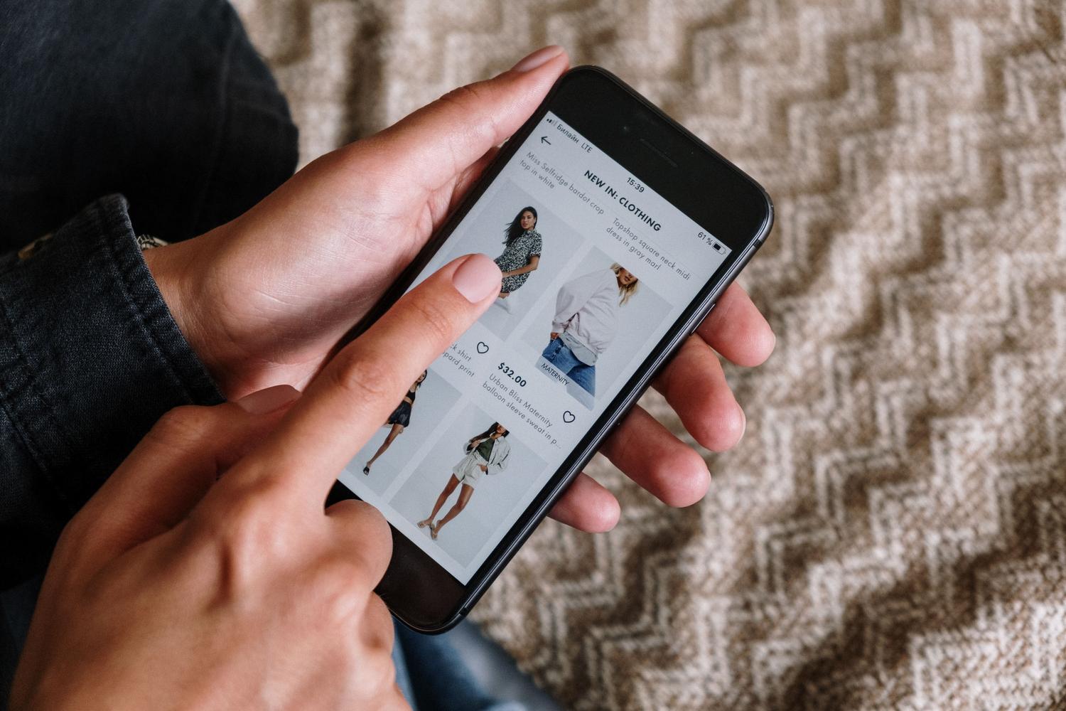Persona navegando por artículos de ropa en un smartphone, ilustrando la experiencia de compra online.