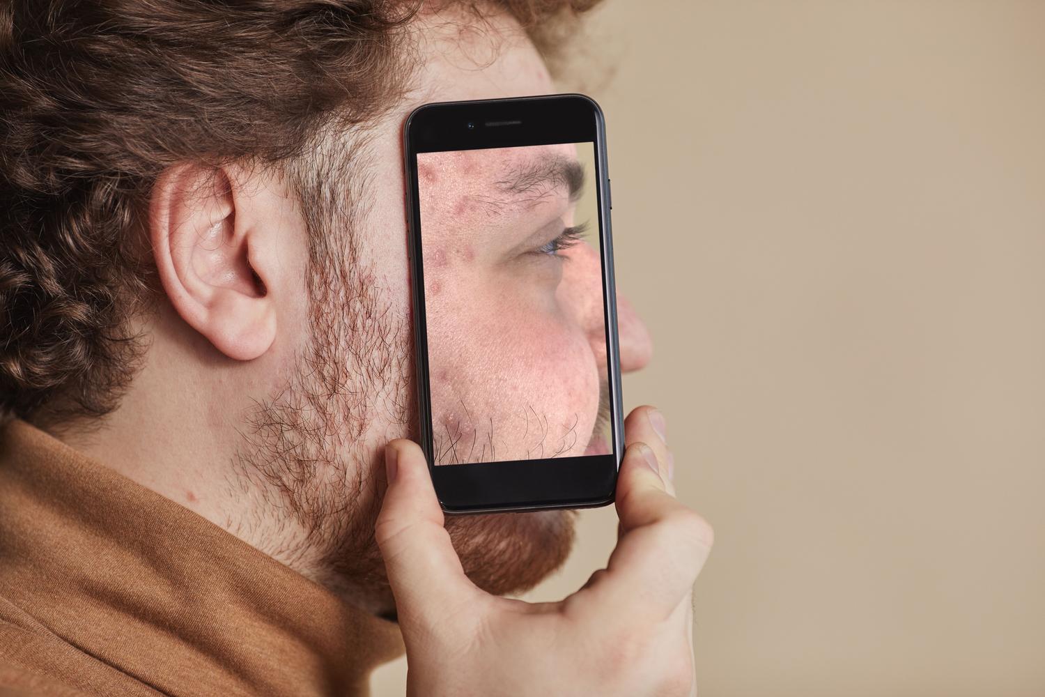 Hombre sosteniendo un smartphone que refleja su rostro, representando el reconocimiento facial.