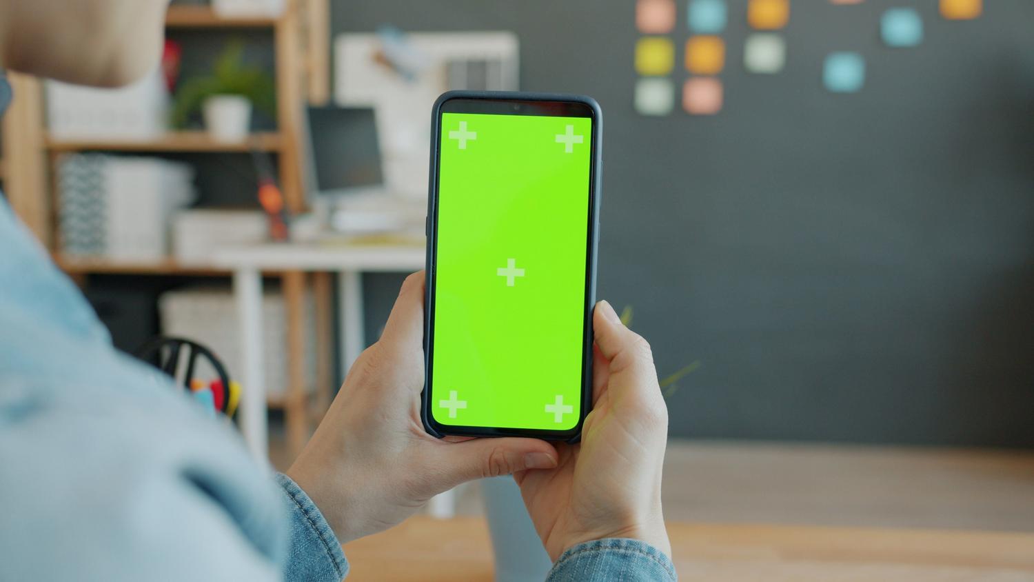 Manos sosteniendo un smartphone en una oficina moderna con notas adhesivas, representando la organización diaria y la productividad.