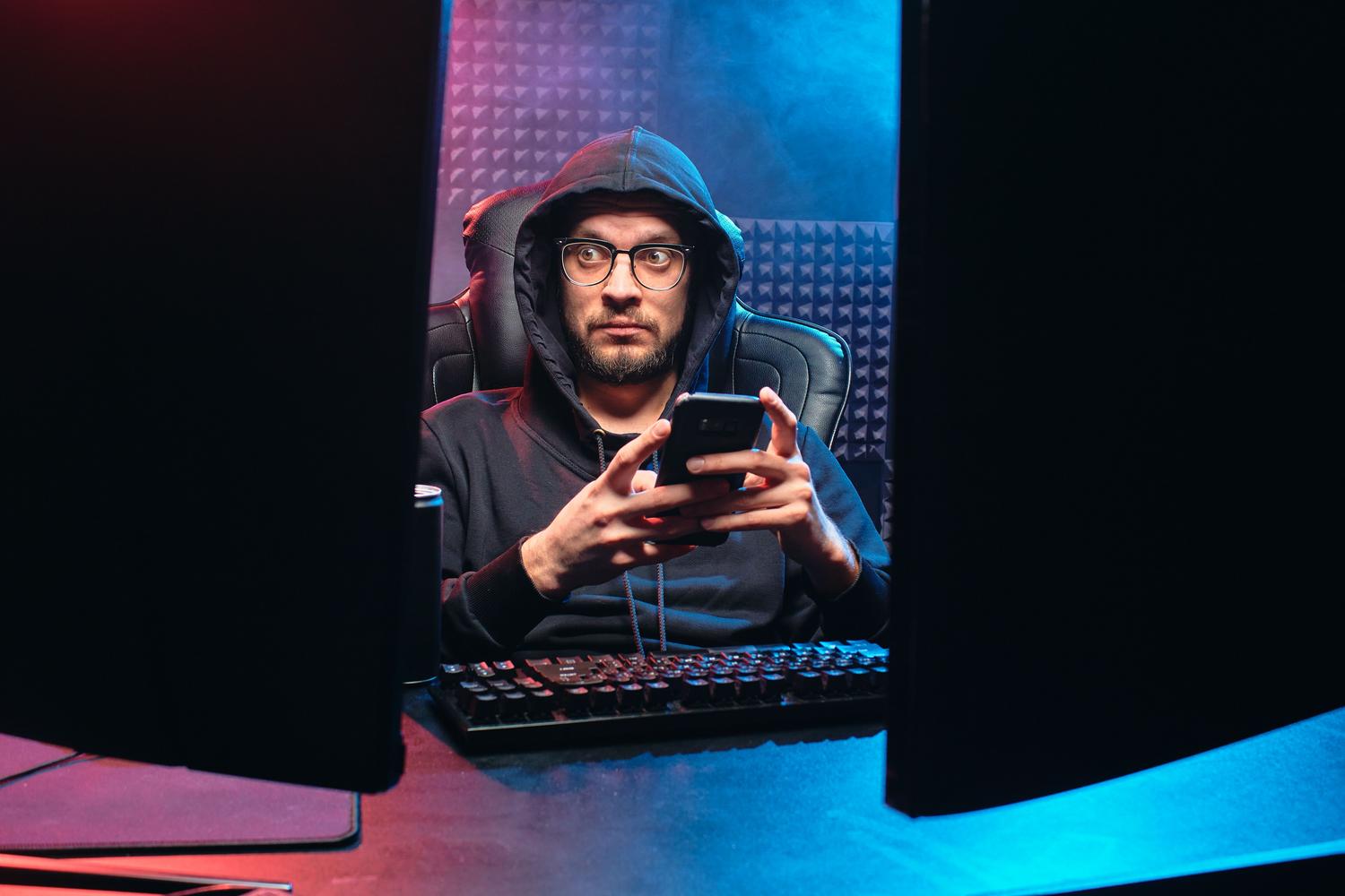 Depiction of a cybercriminal in a dark technological environment using a smartphone to commit fraud. Depiction of a cybercriminal in a dark technological environment using a smartphone to commit fraud.