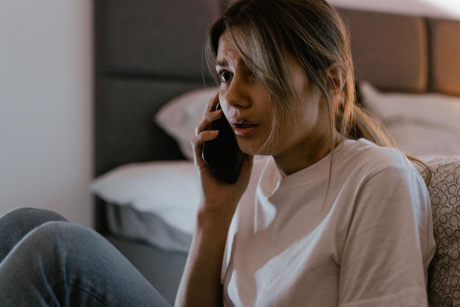 Woman with an expression of anguish and worry while making a phone call, illustrating the emotional pressure of scams. Woman with an expression of anguish and worry while making a phone call, illustrating the emotional pressure of scams.