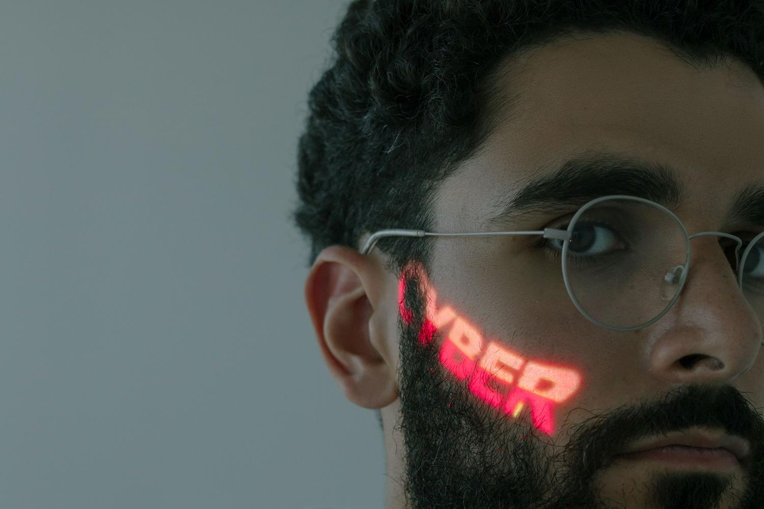 Hombre con gafas y la palabra 'CYBER' proyectada en rojo neón sobre su mejilla, simbolizando la ciberseguridad y la verificación de identidad digital.