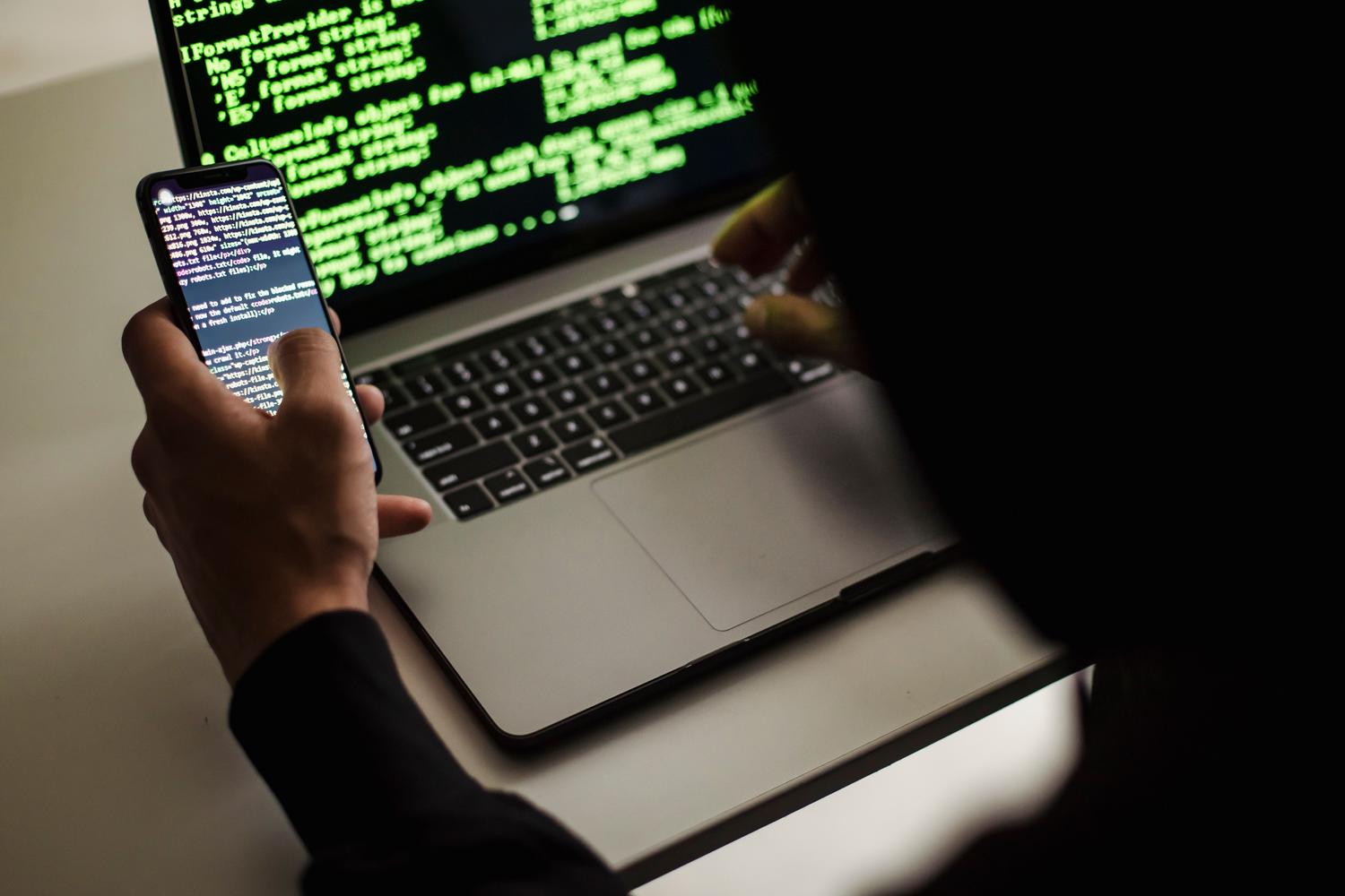 Persona utilizando simultáneamente un ordenador y un móvil, representando la gestión de la identidad digital en múltiples dispositivos.