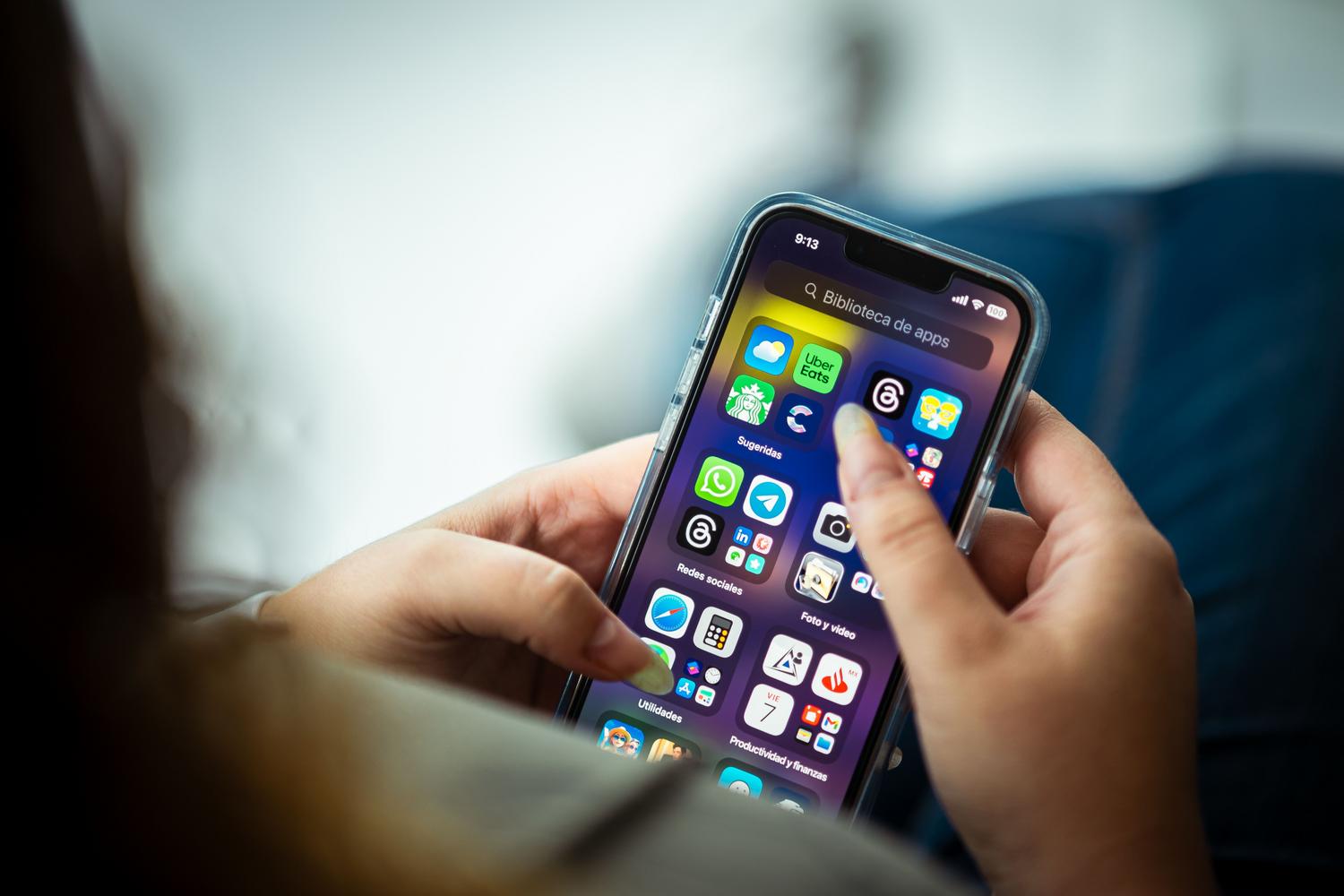 Persona interactuando con la biblioteca de aplicaciones de un iPhone, útil para ilustrar la gestión de notificaciones y ajustes de aplicaciones.