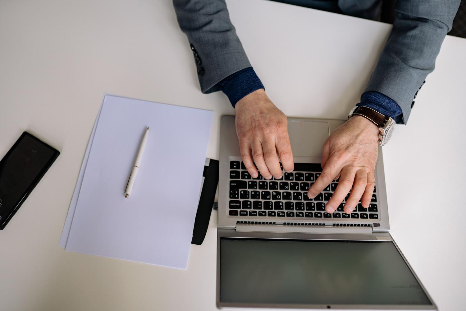 Vista cenital de un profesional trabajando con un portátil y un cuaderno, representando la digitalización de notas analógicas.