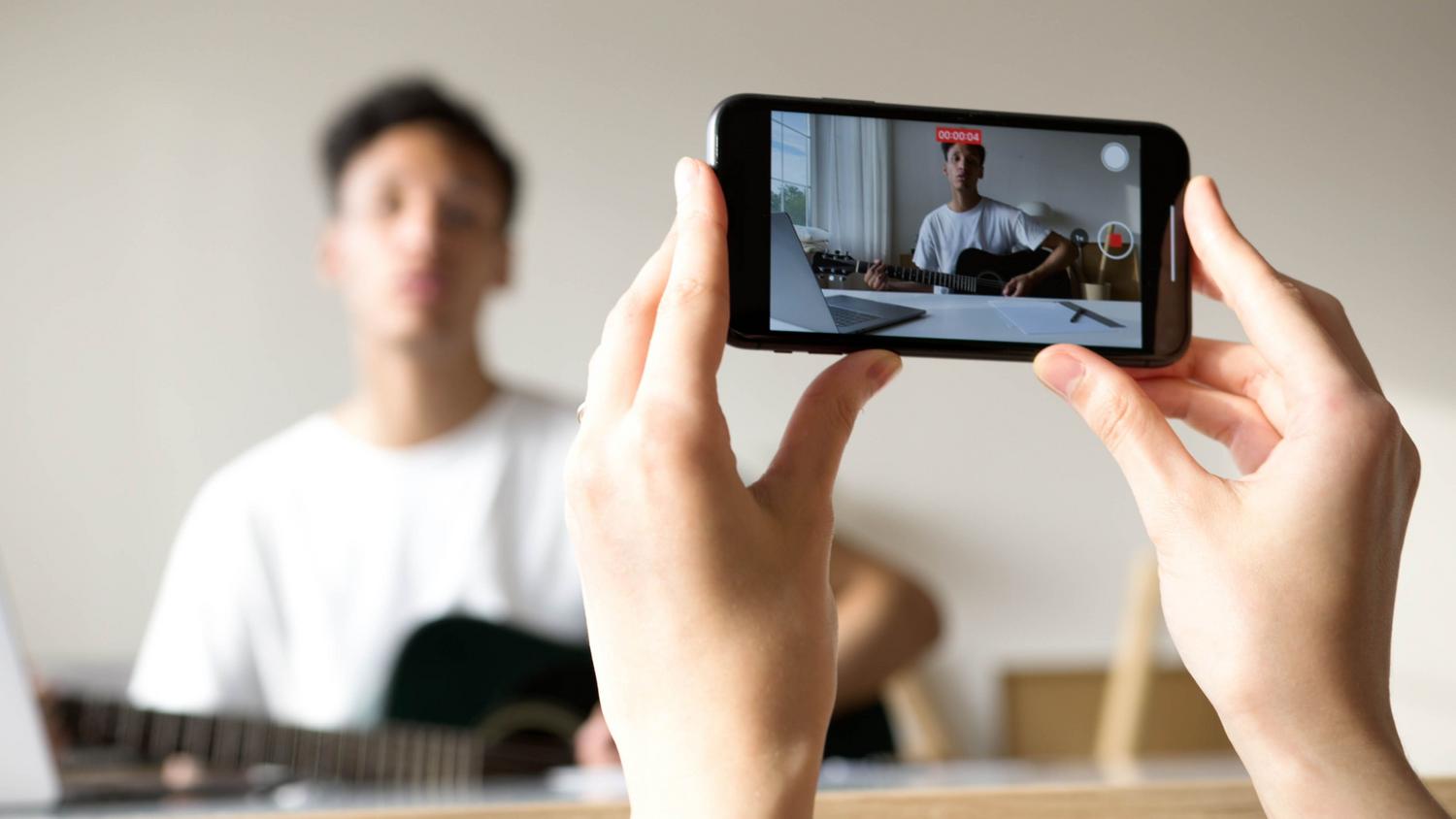 Vista en primera persona de una persona grabando un tutorial de guitarra con un smartphone. Vista en primera persona de una persona grabando un tutorial de guitarra con un smartphone.