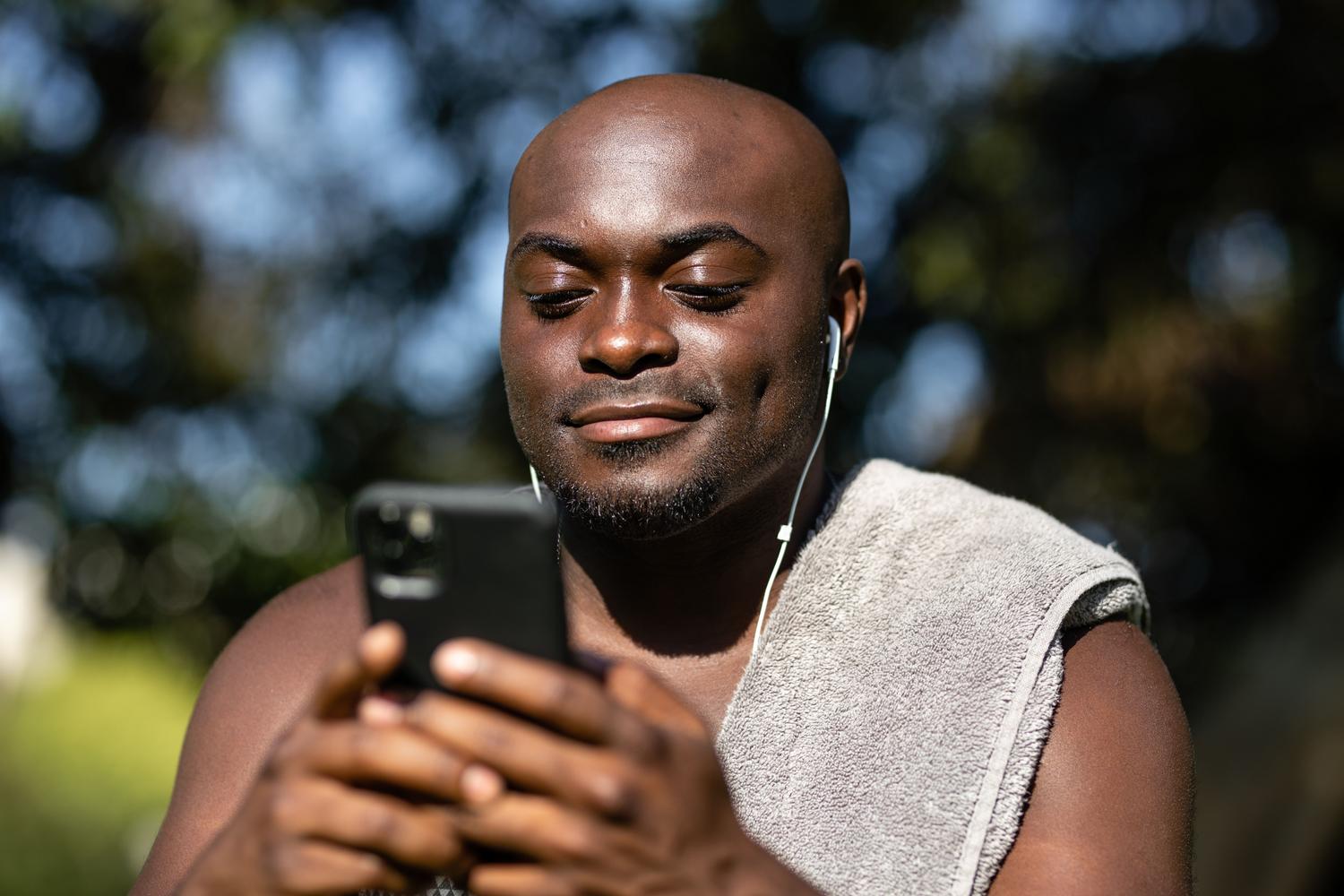 Hombre joven escuchando música con auriculares mientras utiliza su smartphone al aire libre
