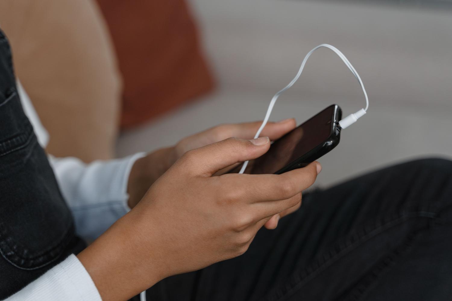 Manos sosteniendo un teléfono móvil con auriculares conectados para escuchar música