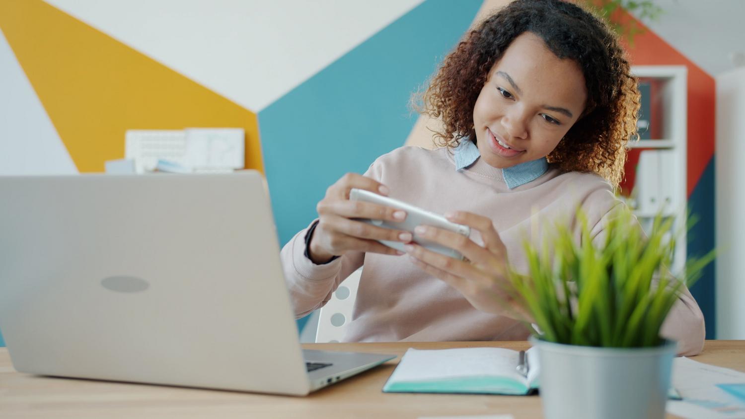 Mujer sonriendo mientras usa su smartphone en un entorno de oficina moderno.