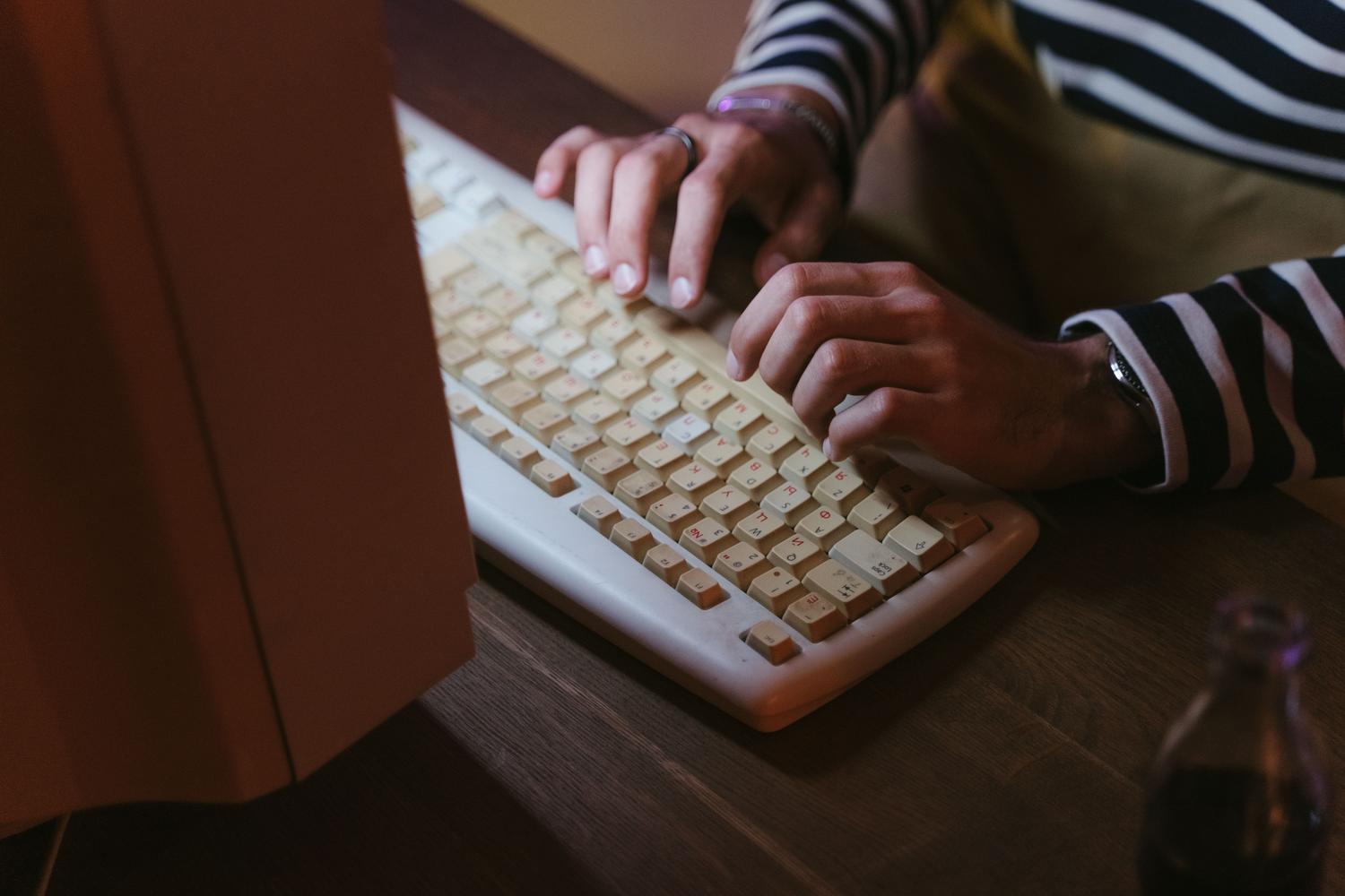 Primer plano de unas manos escribiendo en un teclado mecánico beige de estilo vintage, resaltando la experiencia táctil de la computación retro.