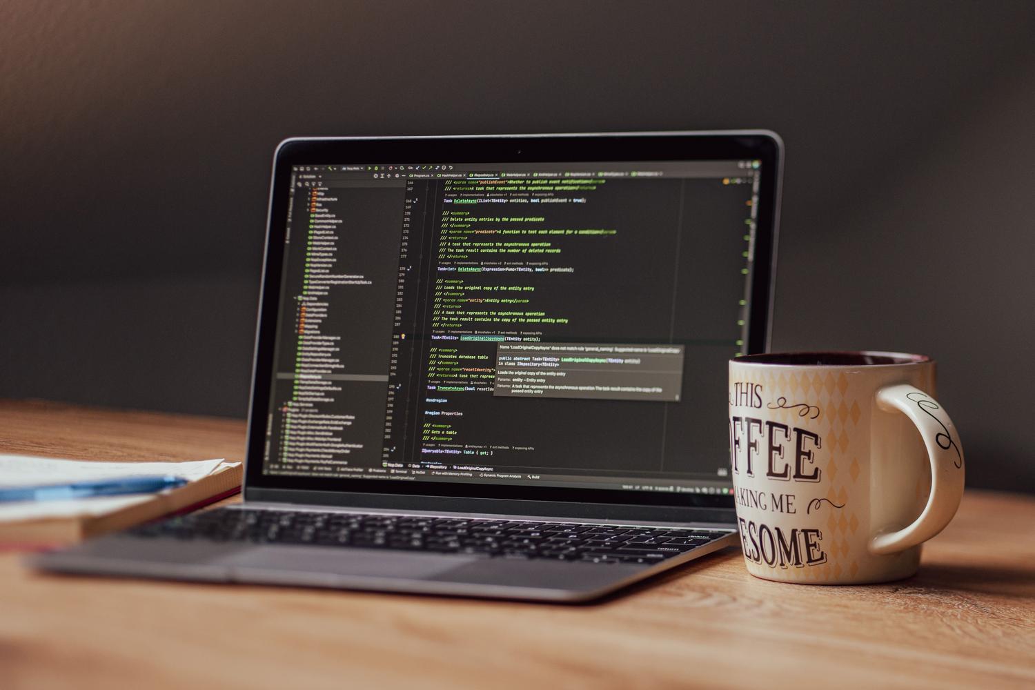 Espai de treball d'un desenvolupador amb un portàtil obert mostrant codi, una tassa de cafè i un quadern, ideal per il·lustrar el procés de configuració de programari.