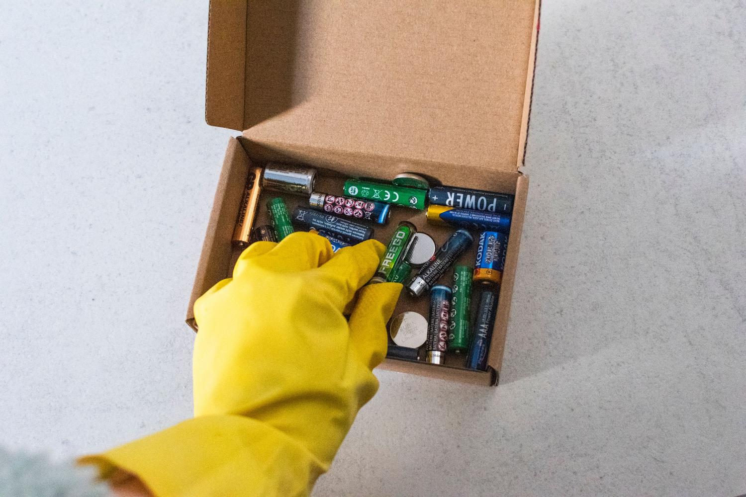 Mano con guantes manipulando baterías usadas para su reciclaje seguro, representando el final de la vida útil de la batería.