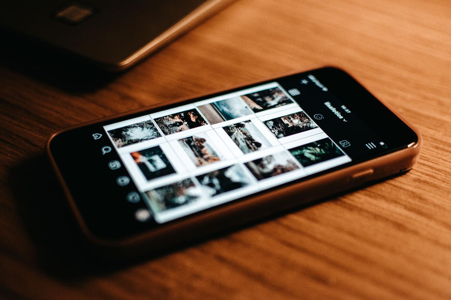 Primer plano de una pantalla de smartphone mostrando una galería de fotos sobre una mesa de madera.