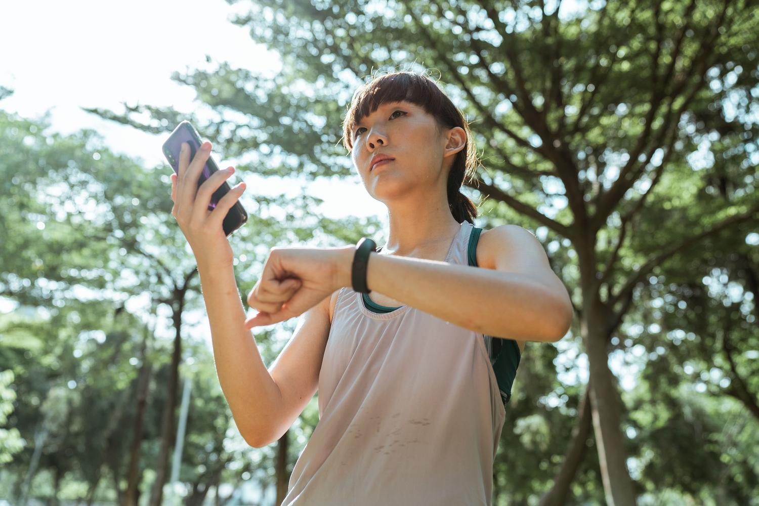 Primer plano de una mujer conectando su smartphone con su reloj inteligente en un entorno natural.