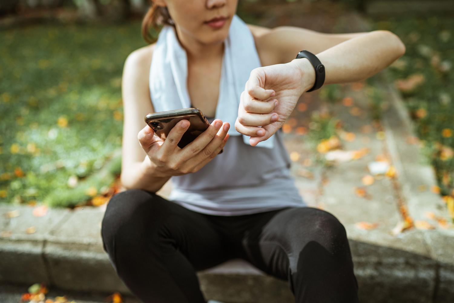 Mujer deportista utilizando simultáneamente un smartphone y un reloj inteligente para monitorizar su actividad física.
