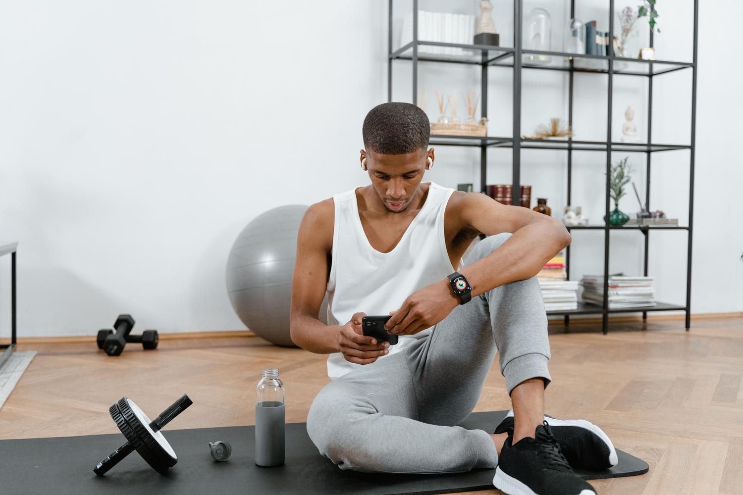 Persona en ropa de deporte utilizando una aplicación de salud en su smartphone mientras descansa sobre una esterilla de yoga.