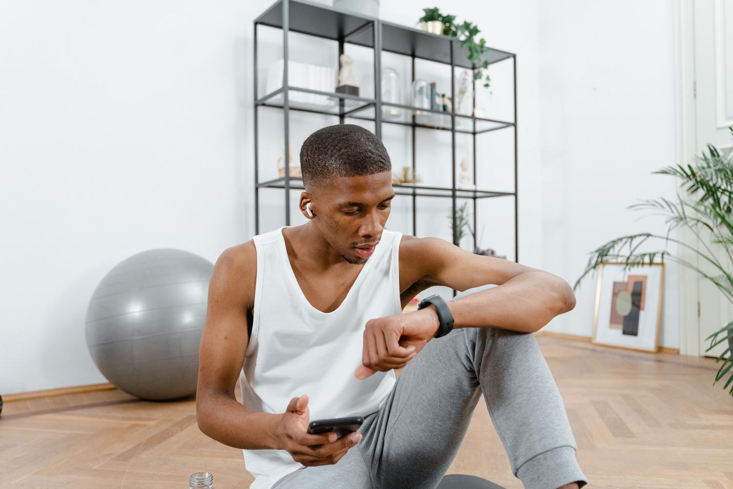 Hombre con ropa deportiva revisando los datos de su smartwatch mientras sostiene un teléfono móvil tras entrenar.