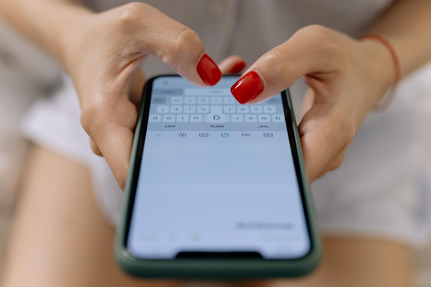 Manos escribiendo en el teclado virtual de un smartphone, mostrando la interfaz de escritura móvil.