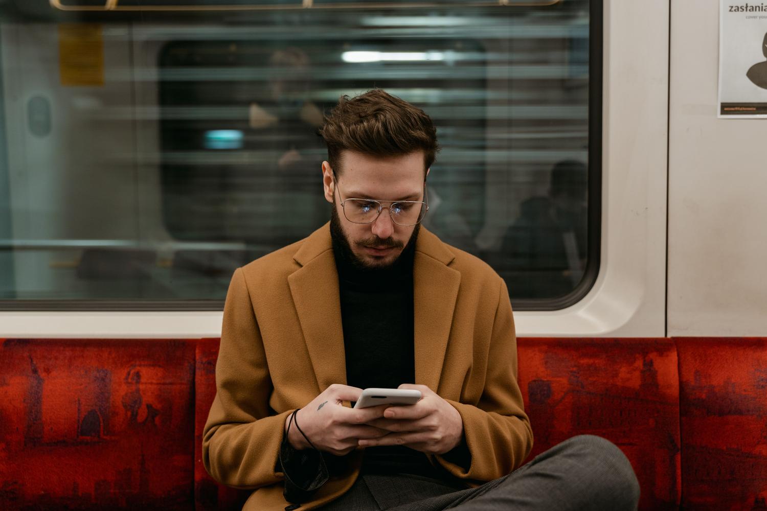 Hombre utilizando su smartphone en el transporte público, ilustrando el riesgo de conectarse a redes WiFi abiertas en entornos urbanos.