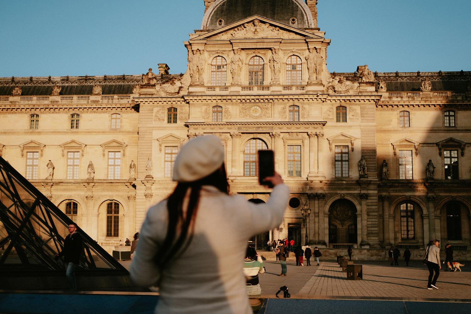 Turista capturando una fotografía del Museo del Louvre en París para obtener información sobre el monumento